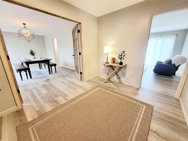 hallway featuring light wood-type flooring, baseboards, and an inviting chandelier