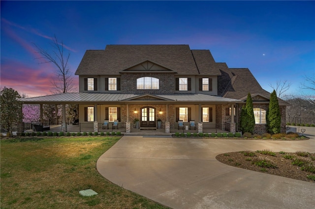 view of front of home with french doors, a standing seam roof, a lawn, curved driveway, and covered porch