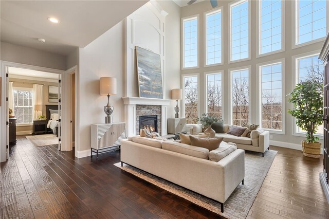 living area with dark wood-style flooring, a high ceiling, a stone fireplace, recessed lighting, and baseboards
