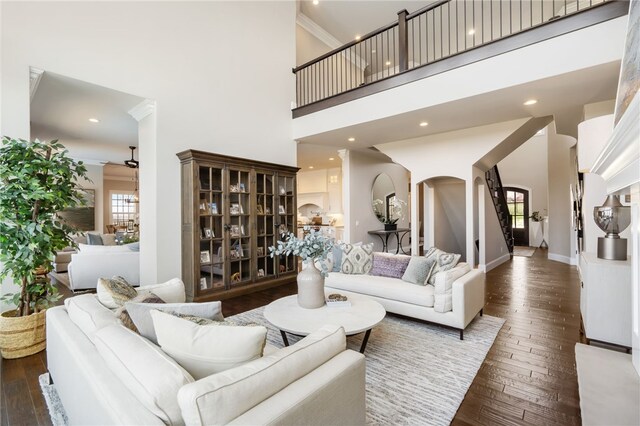 living room featuring wood-type flooring, baseboards, ceiling fan, a high ceiling, and arched walkways
