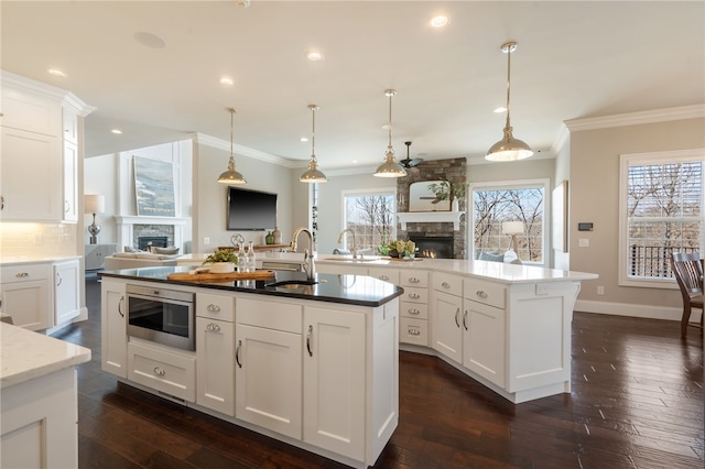 kitchen featuring crown molding, a fireplace, a center island with sink, and a sink