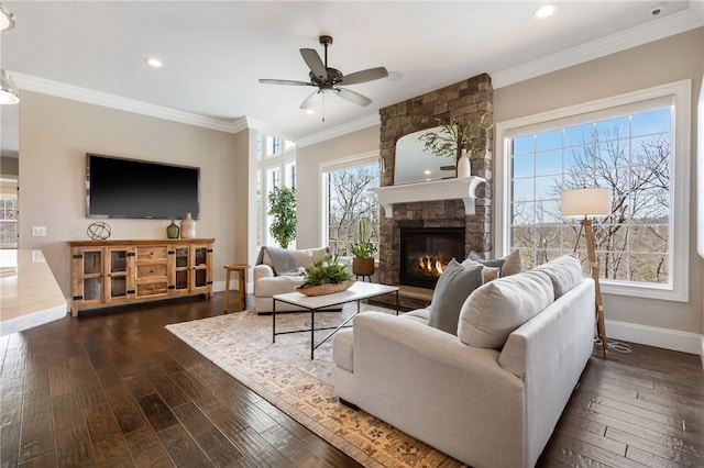living room with ornamental molding, dark wood-style flooring, a stone fireplace, baseboards, and ceiling fan