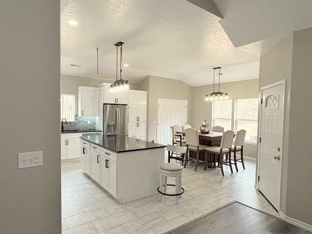 210 Rose Hill Dr, Berryville, AR 72616 - kitchen with dark countertops, lofted ceiling, white cabinetry, stainless steel refrigerator with ice dispenser, and a center island