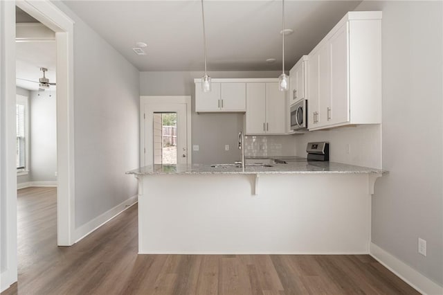 kitchen with white cabinetry, a sink, light stone counters, a peninsula, and appliances with stainless steel finishes