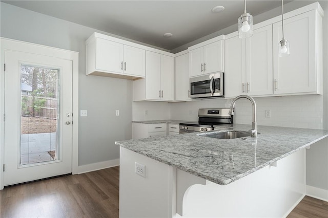 kitchen with stainless steel appliances, dark wood finished floors, a sink, light stone counters, and a peninsula