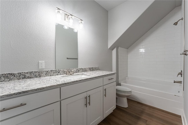 bathroom with wood finished floors, toilet, vanity, a textured wall, and shower / bathtub combination