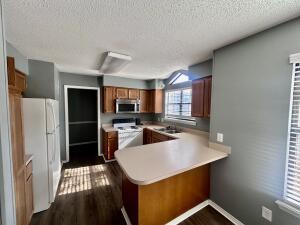 kitchen featuring white appliances, brown cabinetry, a peninsula, light countertops, and dark wood-style floors