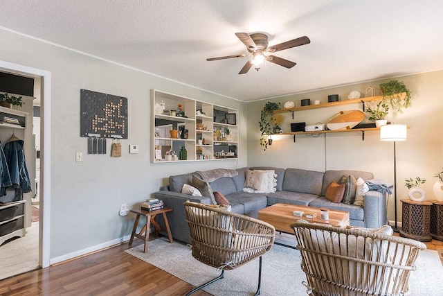 living room featuring a ceiling fan, a textured ceiling, baseboards, and wood finished floors
