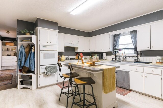 kitchen featuring white cabinets, a kitchen island, under cabinet range hood, and oven
