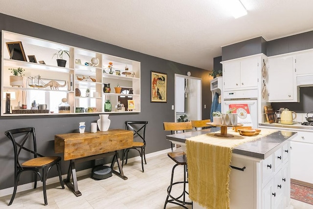 kitchen with white cabinetry, a center island, white oven, and baseboards