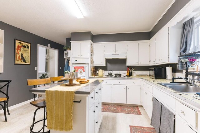 kitchen with light countertops, white appliances, a kitchen island, white cabinetry, and a sink