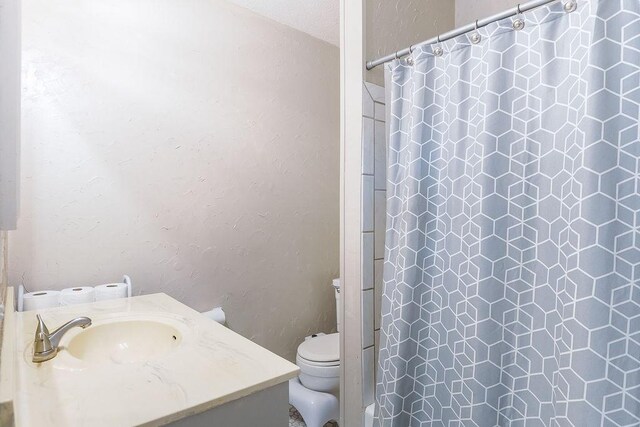 bathroom with toilet, vanity, a textured wall, and curtained shower