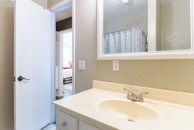 bathroom featuring connected bathroom, a textured wall, a shower with shower curtain, and vanity