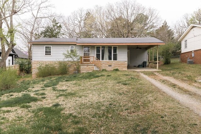 view of front of property featuring stone siding, an attached carport, fence, a front lawn, and dirt driveway