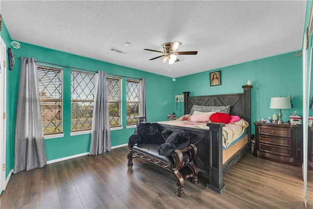 bedroom featuring wood finished floors, a textured ceiling, baseboards, visible vents, and ceiling fan