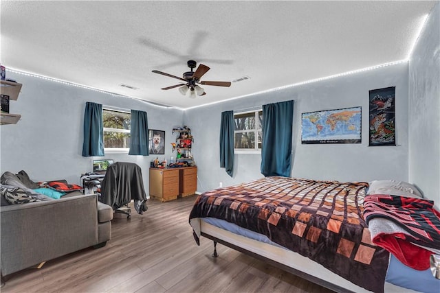 bedroom with a textured ceiling, visible vents, a ceiling fan, and wood finished floors
