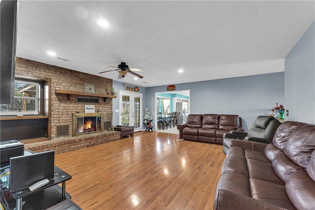 living room with a textured ceiling, visible vents, a brick fireplace, ceiling fan, and wood finished floors