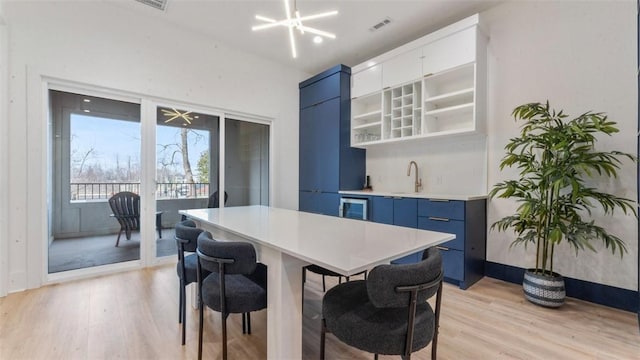 225 SE 7th St, Bentonville, AR 72712 - kitchen featuring blue cabinetry, light wood-type flooring, a kitchen bar, modern cabinets, and a sink