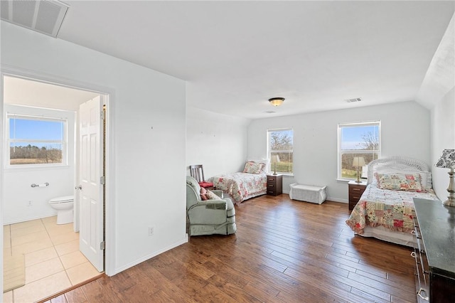 bedroom featuring wood finished floors, baseboards, ensuite bathroom, and visible vents