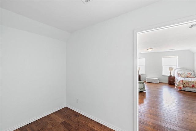 empty room featuring wood-type flooring, baseboards, lofted ceiling, and visible vents