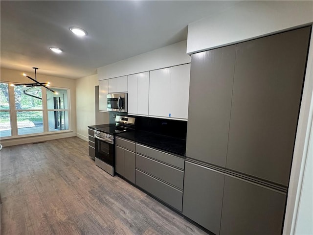kitchen with a chandelier, wood finished floors, appliances with stainless steel finishes, dark countertops, and white cabinets