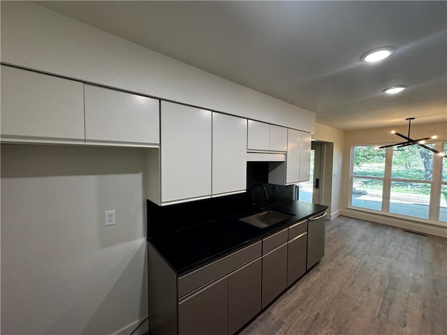 kitchen featuring wood finished floors, dark countertops, white cabinetry, a sink, and stainless steel dishwasher
