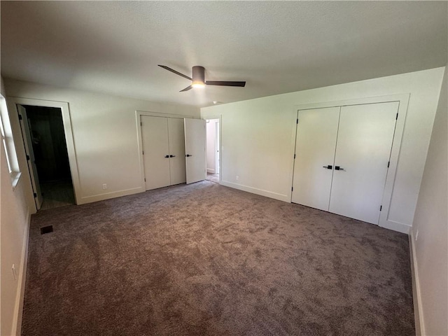 unfurnished bedroom with baseboards, two closets, carpet, and a ceiling fan