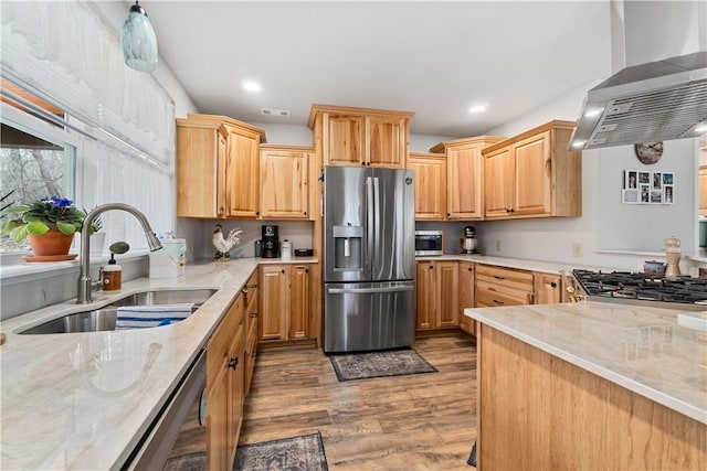 kitchen with a sink, light stone countertops, wood finished floors, stainless steel appliances, and wall chimney range hood