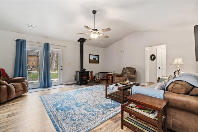 living room with visible vents, light wood-style flooring, vaulted ceiling, a ceiling fan, and a wood stove