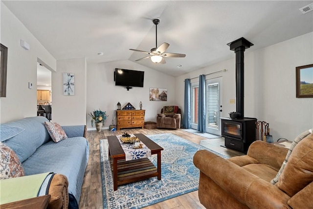 living room with vaulted ceiling, a wood stove, light wood-style floors, ceiling fan, and visible vents