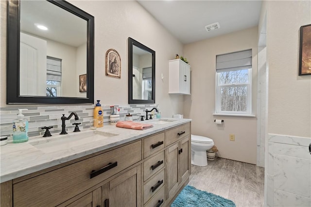 bathroom with double vanity, tasteful backsplash, toilet, and a sink