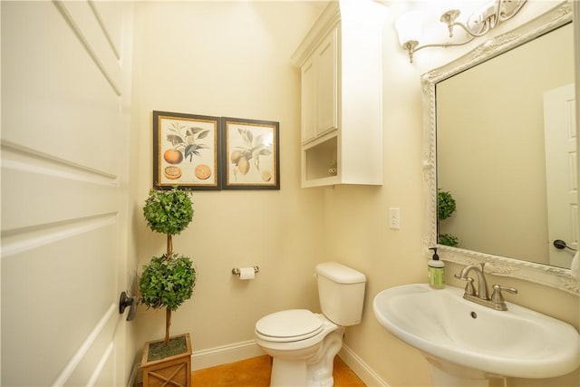 half bathroom with a sink, tile patterned flooring, toilet, and baseboards
