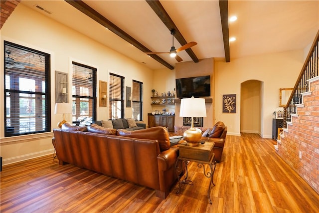 living room with a ceiling fan, baseboards, wood finished floors, arched walkways, and beam ceiling