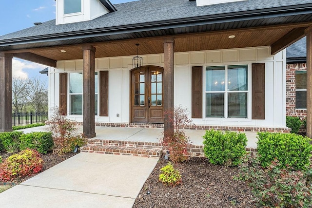 view of exterior entry with a porch, roof with shingles, and board and batten siding