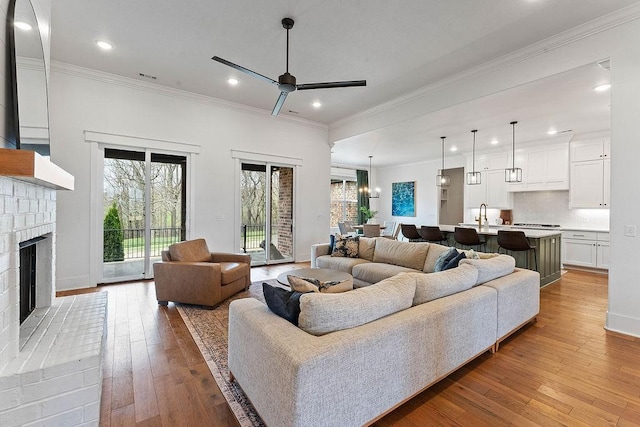 living area with crown molding, ceiling fan, recessed lighting, a brick fireplace, and light wood finished floors
