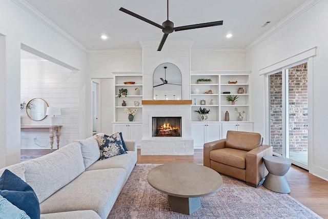 living room featuring a brick fireplace, a ceiling fan, ornamental molding, and wood finished floors