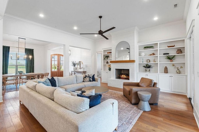 living room with ceiling fan with notable chandelier, a fireplace, light wood-type flooring, ornamental molding, and visible vents