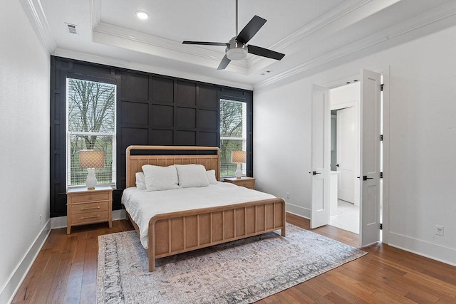 bedroom with baseboards, crown molding, visible vents, a raised ceiling, and wood-type flooring