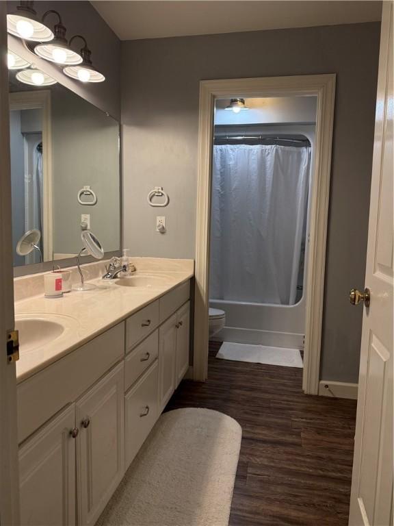 2110 W 8th St, Russellville, AR 72801 - bathroom featuring double vanity, toilet, wood finished floors, shower / bathtub combination with curtain, and baseboards