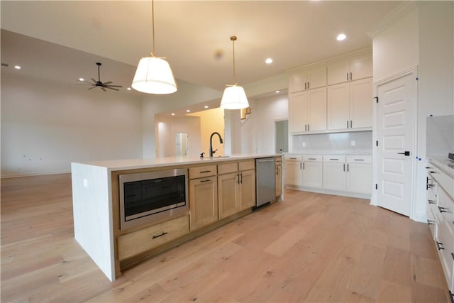 kitchen with stainless steel dishwasher, an island with sink, light countertops, built in microwave, and light wood-style flooring
