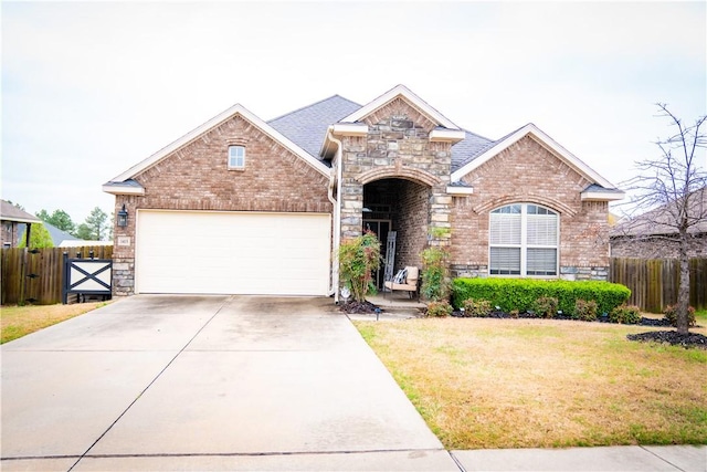 view of front of property featuring a front yard, driveway, stone siding, an attached garage, and fence