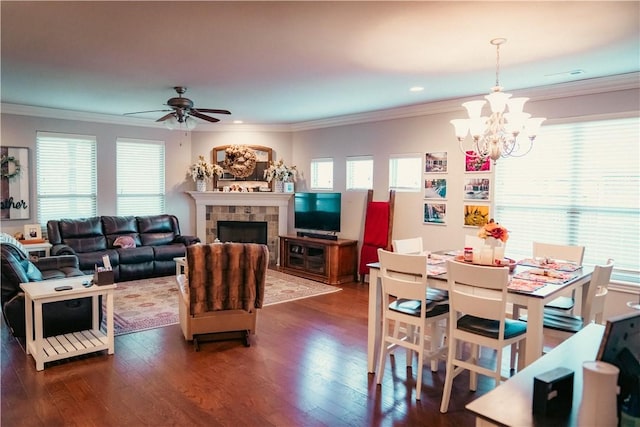 living area featuring ornamental molding, ceiling fan with notable chandelier, a tiled fireplace, and dark wood-type flooring
