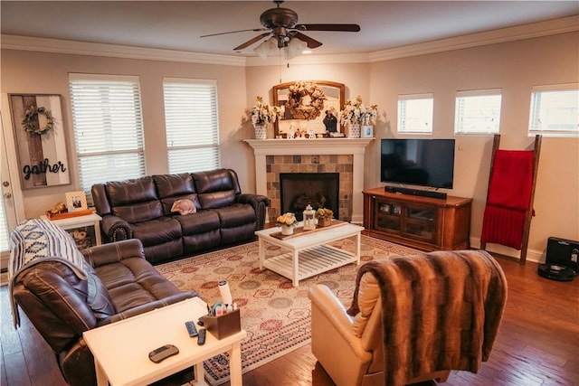 living area with ceiling fan, a tiled fireplace, hardwood / wood-style floors, and ornamental molding