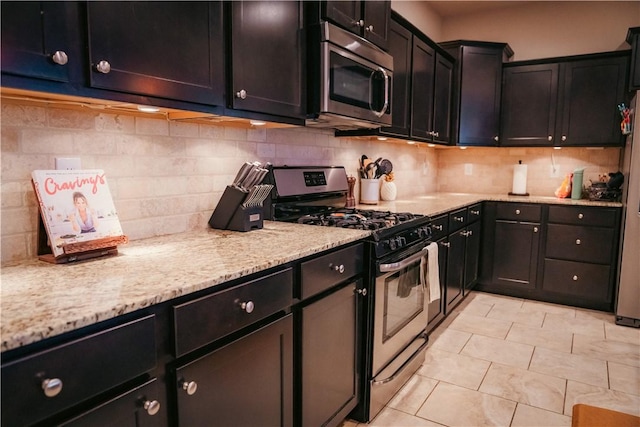 kitchen with tasteful backsplash, light tile patterned floors, light stone countertops, and appliances with stainless steel finishes