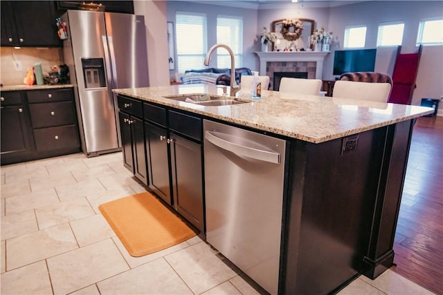 kitchen featuring a sink, a tiled fireplace, stainless steel appliances, crown molding, and open floor plan