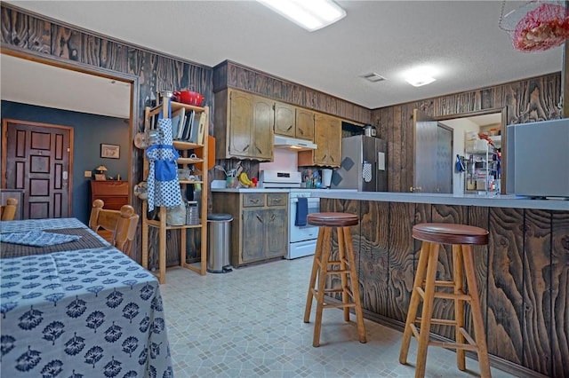 1812 E 12th St, Russellville, AR 72802 - kitchen featuring white gas stove, stainless steel fridge with ice dispenser, under cabinet range hood, wood walls, and light floors
