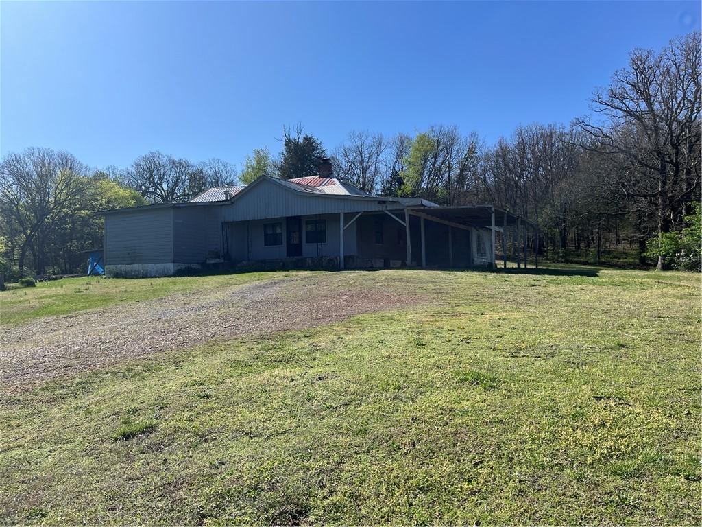 view of front facade with a front yard, dirt driveway, metal roof, and a chimney