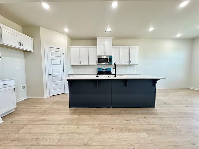 4903 SW Wakanda St, Bentonville, AR 72713 - kitchen featuring stainless steel microwave, white cabinets, light countertops, range, and light wood-style flooring