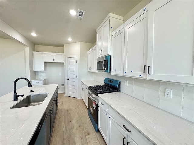4903 SW Wakanda St, Bentonville, AR 72713 - kitchen featuring appliances with stainless steel finishes, light wood-style floors, recessed lighting, white cabinets, and tasteful backsplash