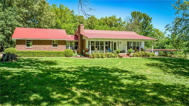 back of house featuring a chimney, metal roof, covered porch, and a lawn